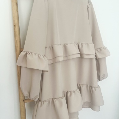 Vestido beige claro com folhos e mangas longas pendurado numa escada de madeira