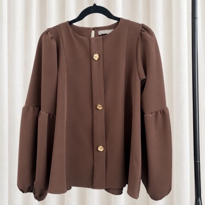 Blusa castanha com botões dourados pendurada num cabide