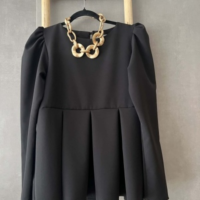 Blusa preta com pregas e colar dourado pendurado no cabide numa escada de madeira