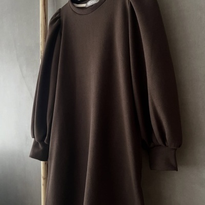 Vestido castanho escuro com mangas bufantes pendurado num cabide negro numa estrutura de madeira