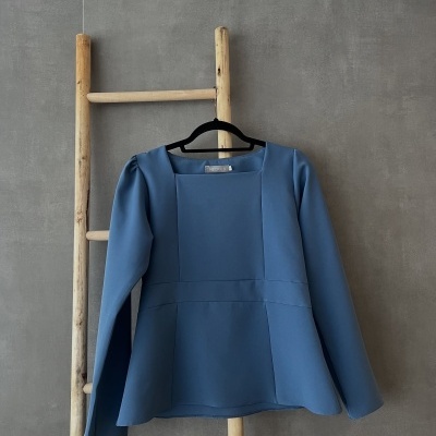 Blusa azul com decote quadrado numa escada de madeira against parede cinza