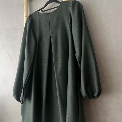 Vestido verde escuro de manga comprida pendurado em cabide numa estrutura de madeira