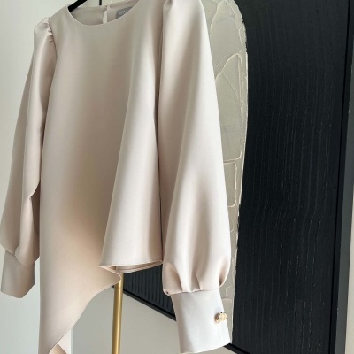 Blusa creme com mangas bufantes e botões dourados pendurada num cabide
