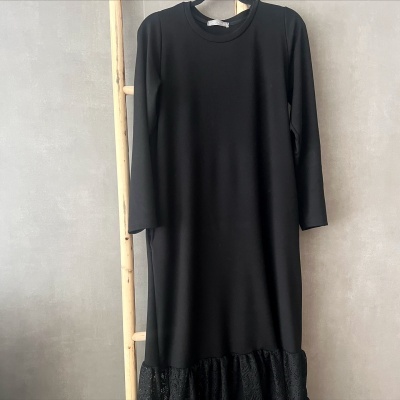 Vestido preto com renda preta na barra pendurado numa estrutura de madeira