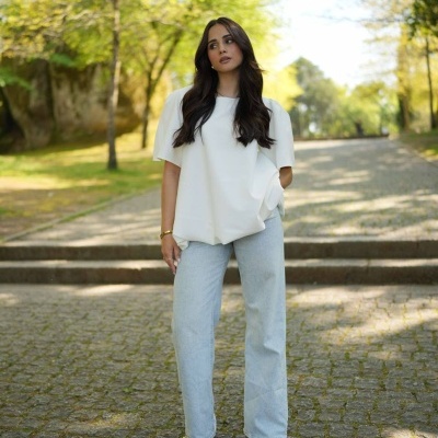 Mulher com t-shirt branca e calças de ganga azuis claras em área exterior pavimentada e ensolarada