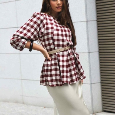 Mulher com blusa xadrez vinho e creme e cinto bege, saia creme, em ambiente urbano