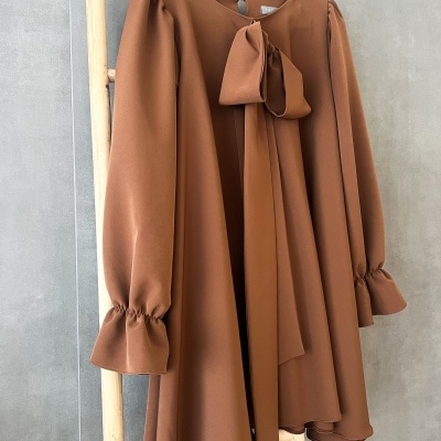 Vestido castanho claro com laço e mangas compridas pendurado num cabide