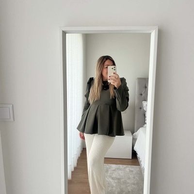 Mulher a tirar selfie num espelho de moldura branca, blusa verde e calças brancas largas.