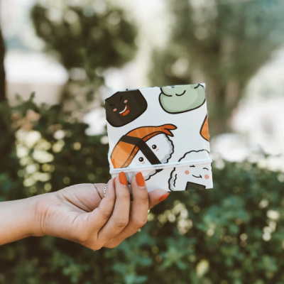 Carteira de tecido com padrão de sushi sorridente em fundo desfocado verde