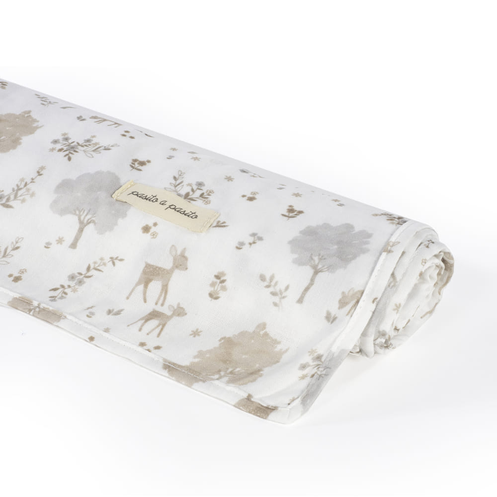 Tecido branco com estampado de cervos, árvores e plantas em tons neutros enrolado