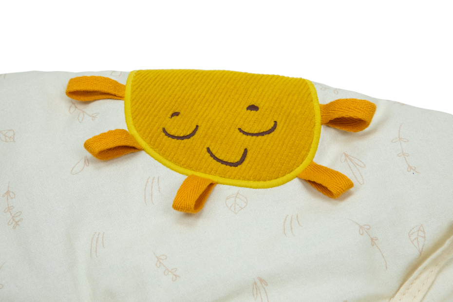 Manta branca com padrão de folhas e aplicação amarela em forma de sol com rosto sorridente