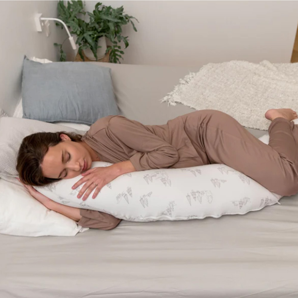 Mulher a dormir abraçando travesseiro de corpo branco com padrão cinza sobre cama cinza claro