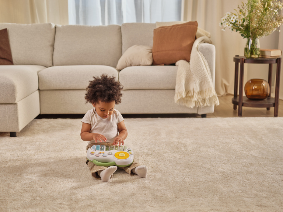 Criança com brinquedo musical sentada em tapete com sofá e mesa em sala acolhedora