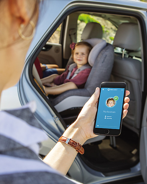 Criança na cadeira auto dentro de carro prateado, telemóvel com ecrã azul e nome 'Mia Beckham'