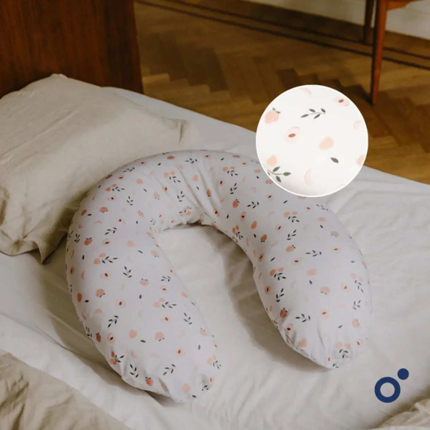 Travesseiro em forma de U com padrão floral rosa e preto sobre fundo branco numa cama de lençóis bege