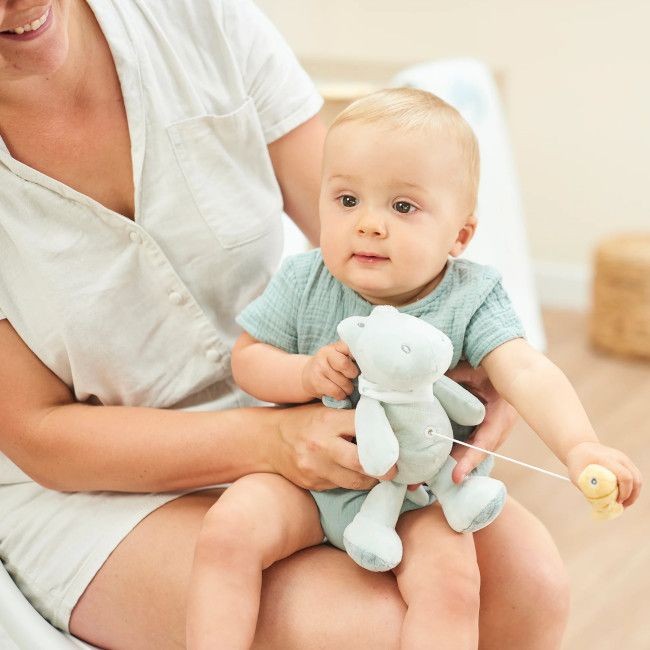 Bebé com brinquedo de peluche azul sentado no colo de um adulto com roupa branca