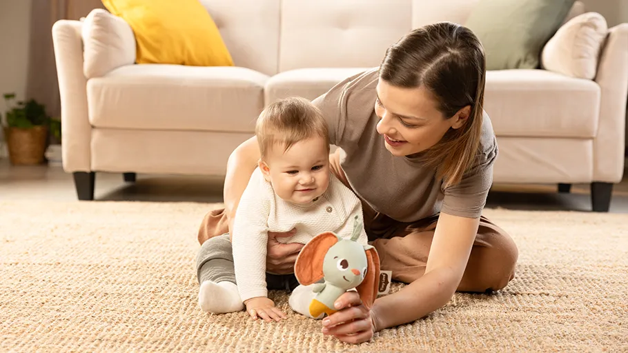Bebé e mulher a brincar no tapete com brinquedo de peluche colorido