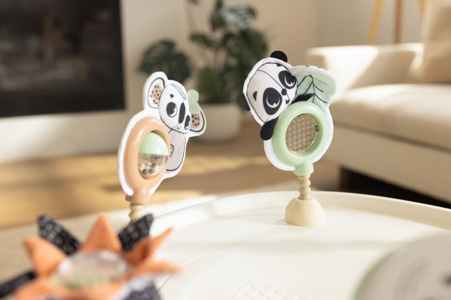 Brinquedos de bebé com pandas em tecido e plástico pastel numa superfície branca