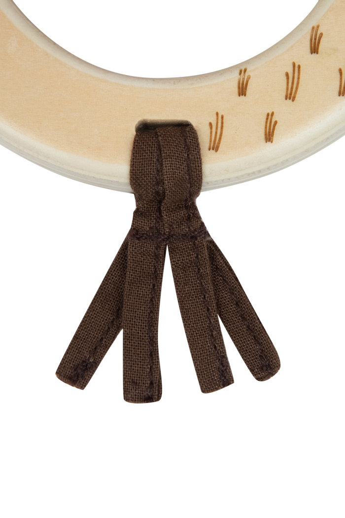 Detalhe de objeto circular claro com decoração castanha e tiras de tecido castanho penduradas