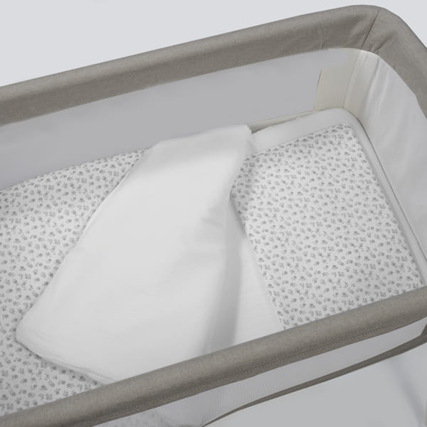 Berço portátil com colchão com padrão de pequenas flores cinzentas e lençol branco