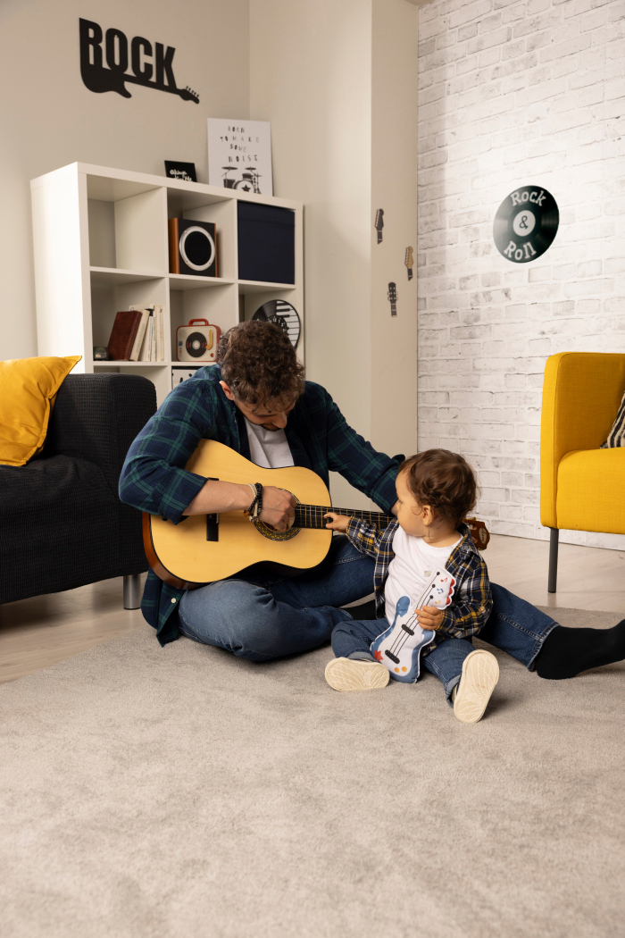 Homem e criança com guitarras sentados em tapete numa sala decorada com elementos rock