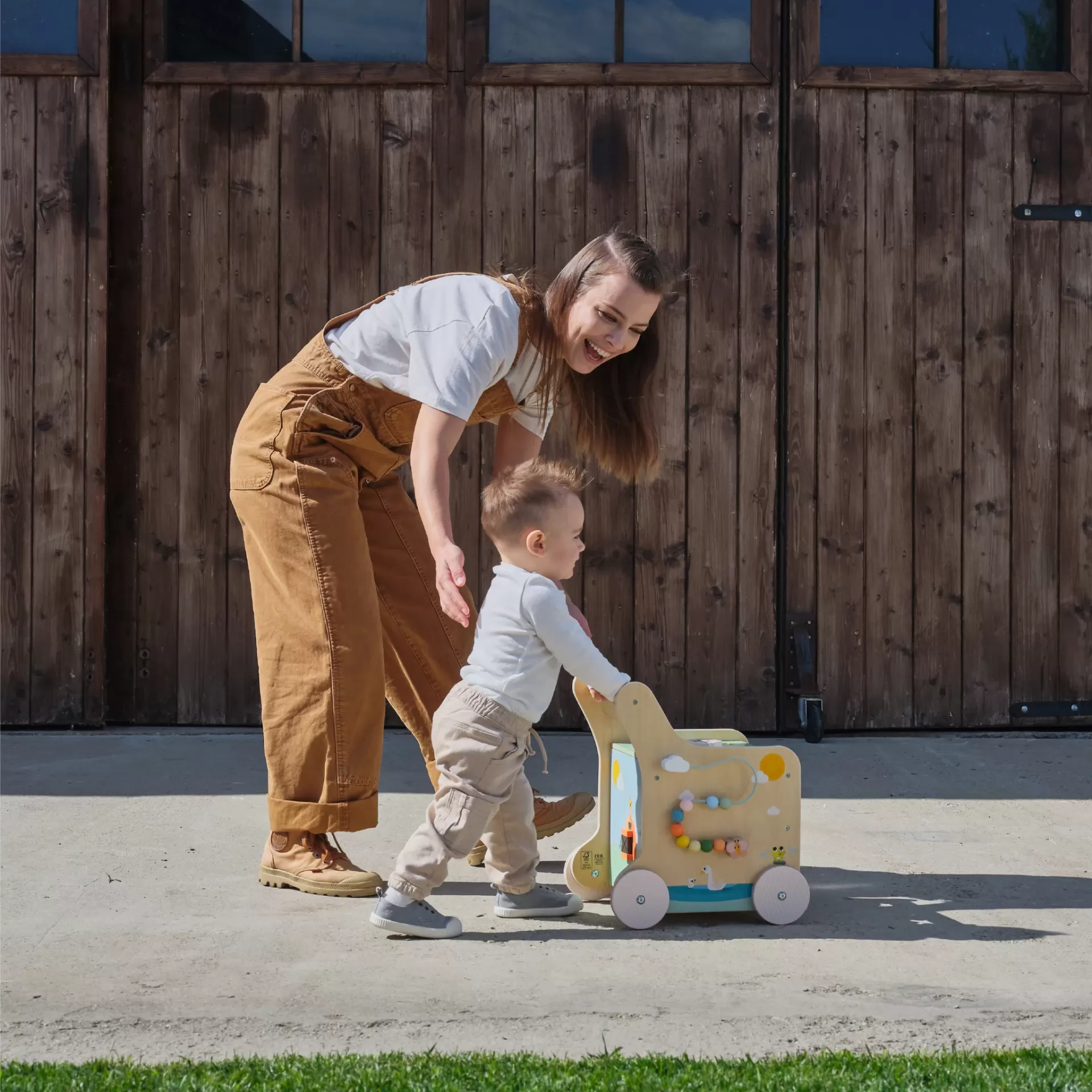 Caminhador infantil de madeira com desenhos coloridos e criança a usá-lo em ambiente exterior