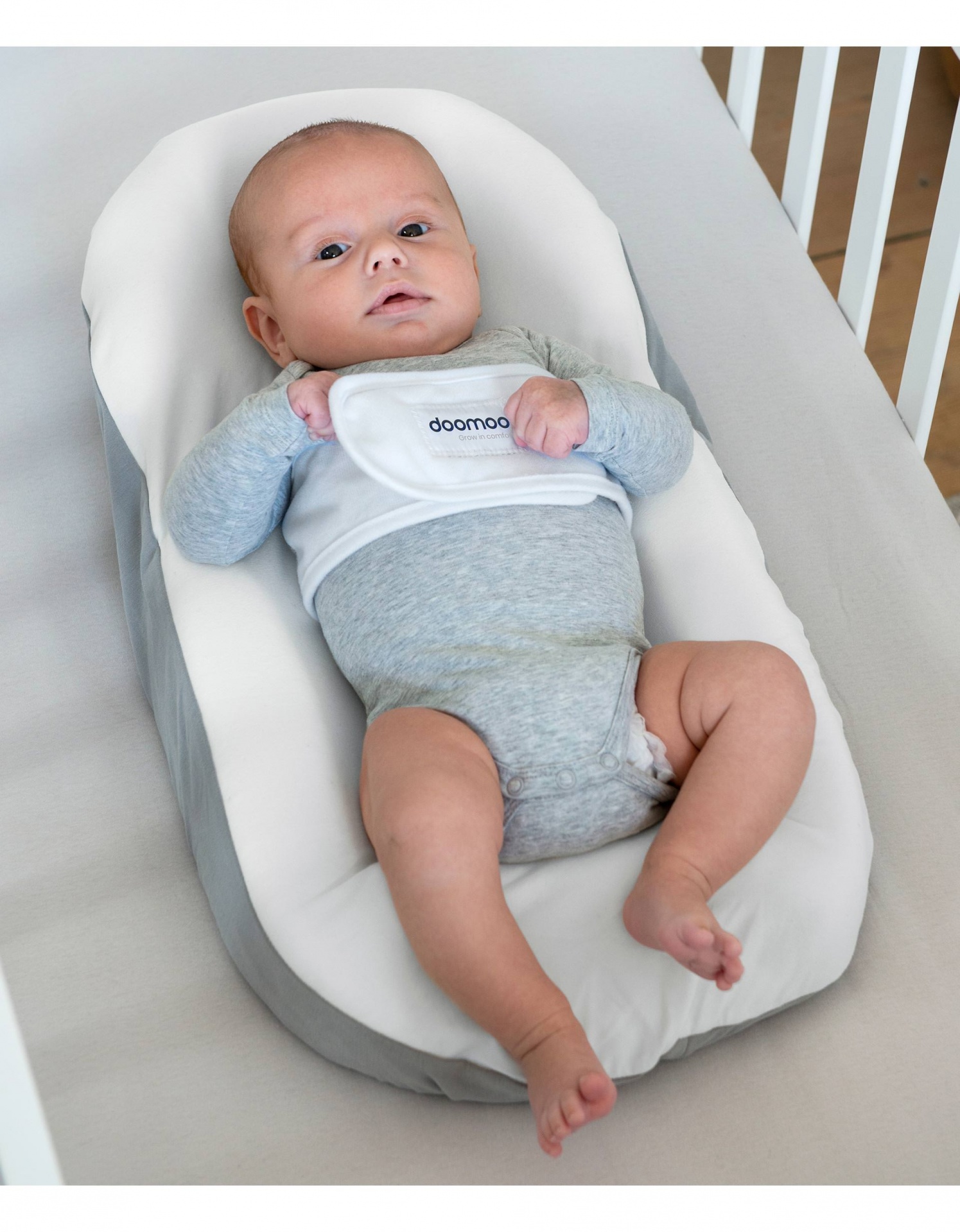 Bebé deitado em almofada ergonómica branca e cinza no berço