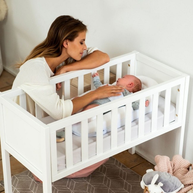 Berço branco de madeira com bebé e mulher ao lado