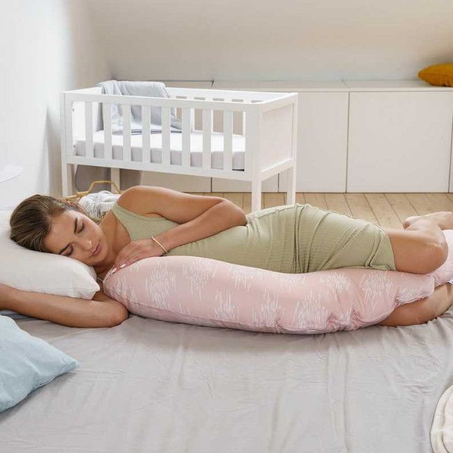 Mulher a dormir abraçando almofada de corpo rosa com padrão branco numa cama cinza