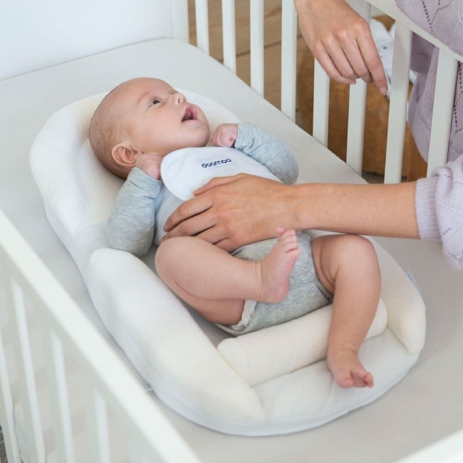 Bebé deitado em cadinho branco acolchoado dentro de berço branco
