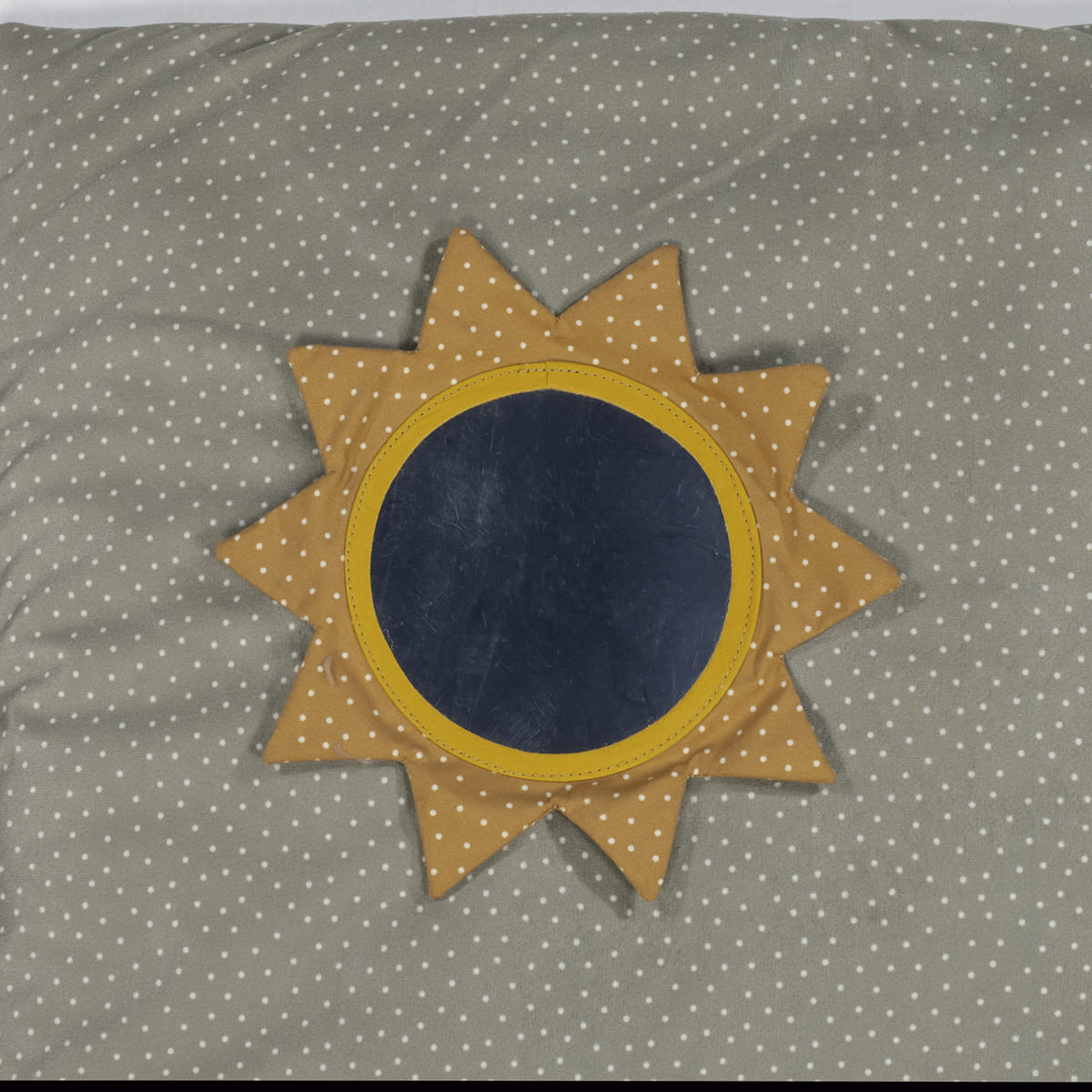 Almofada em forma de sol sobre colchão cinzento com estrelas brancas