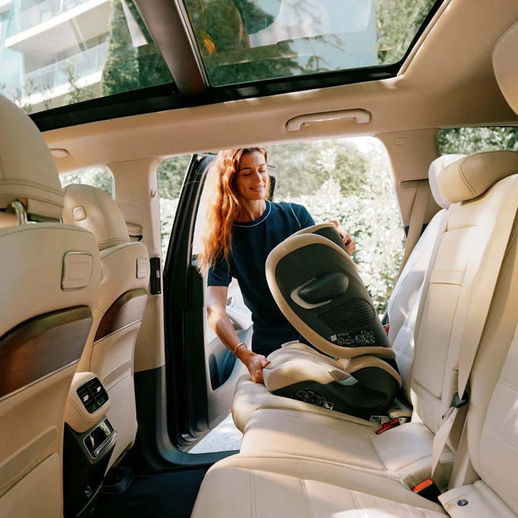 Cadeira de carro para bebé preta no banco traseiro de um carro com estofos bege e teto panorâmico