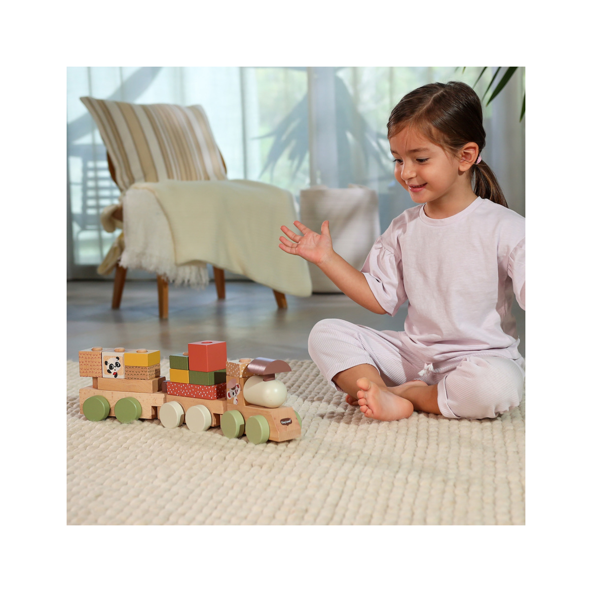 Comboio de madeira colorido com peças empilháveis e criança sentada ao lado num tapete