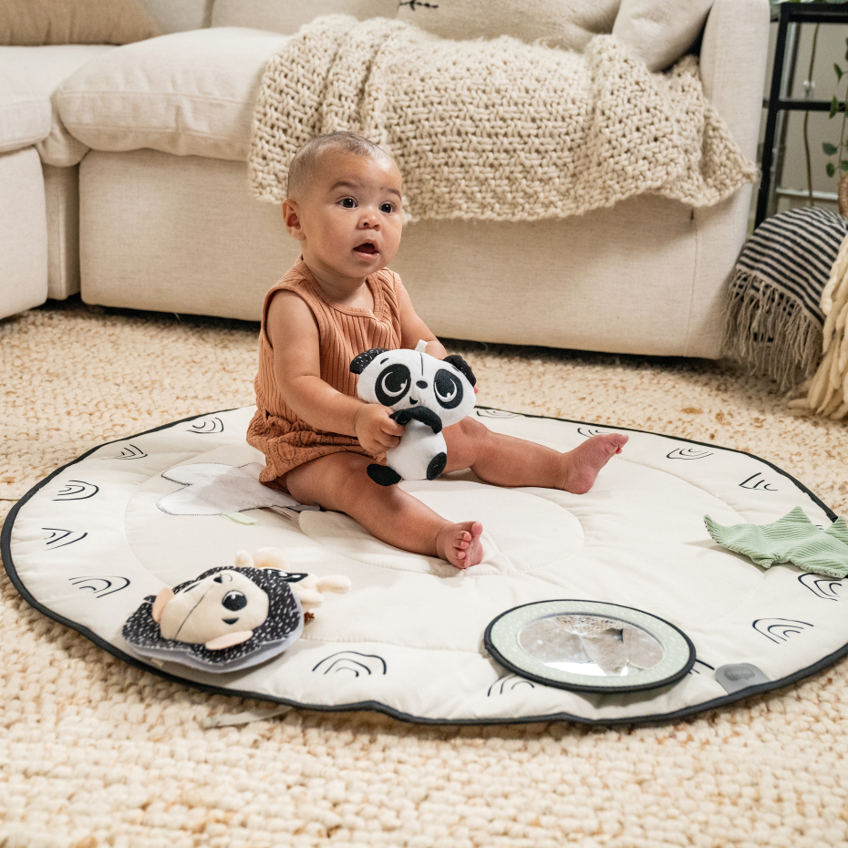 Bebé num tapete redondo acolchoado com brinquedos e sofá ao fundo