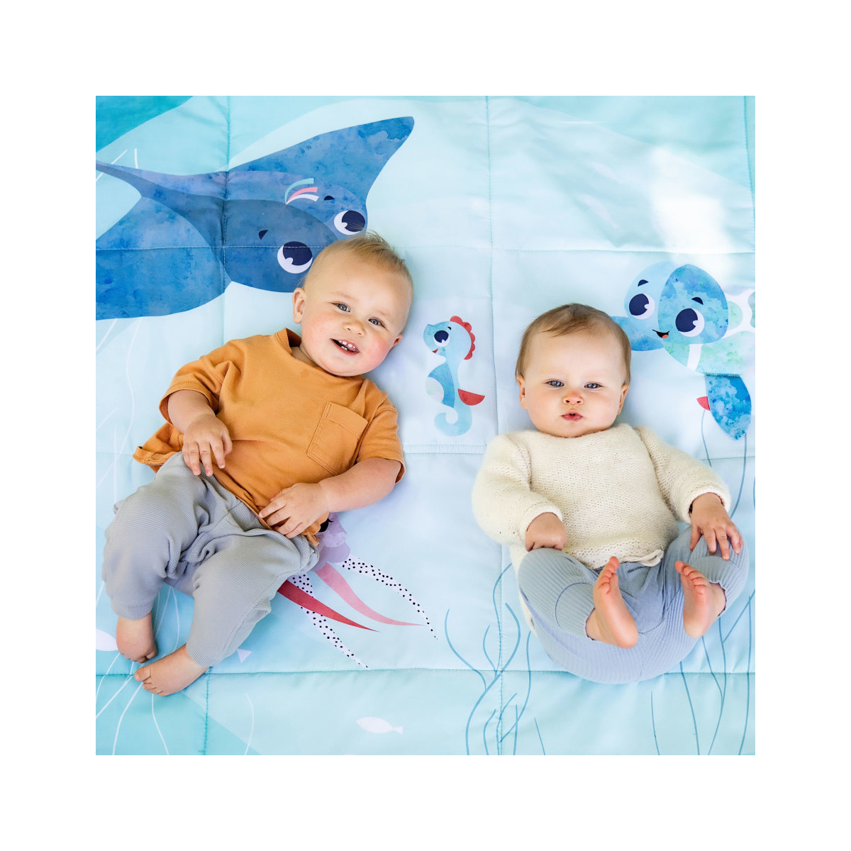 Dois bebés deitados sobre tapete com desenhos de animais marinhos azuis