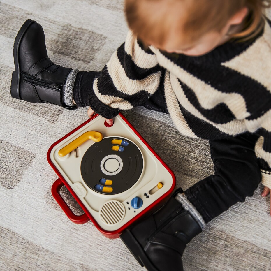 Criança com botas pretas e camisola às riscas a brincar com gira-discos de brinquedo