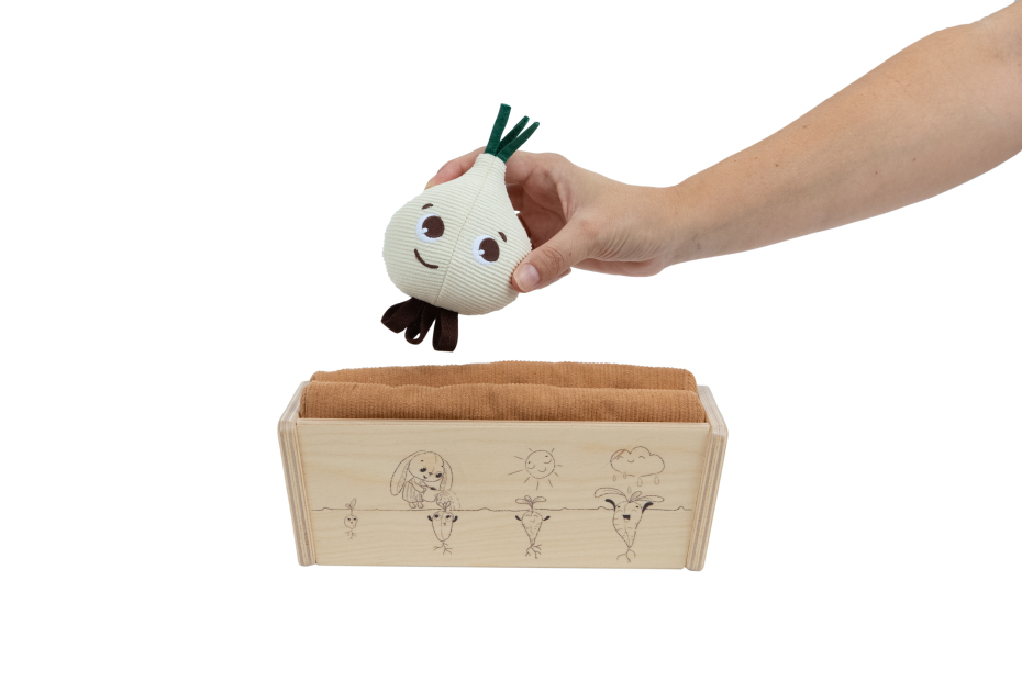 Brinquedo macio em forma de cebola com rosto sorridente sobre caixa de madeira clara com toalha castanha