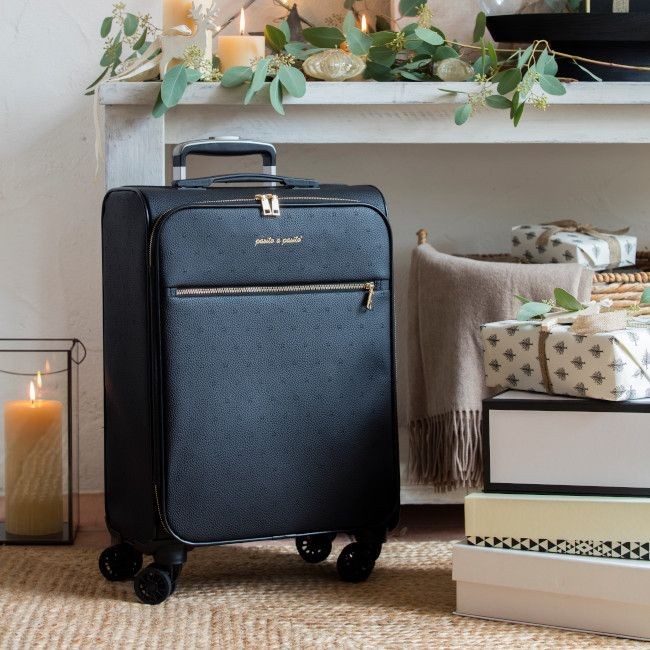 Mala de viagem preta com rodinhas, perto de velas e presentes num ambiente interior