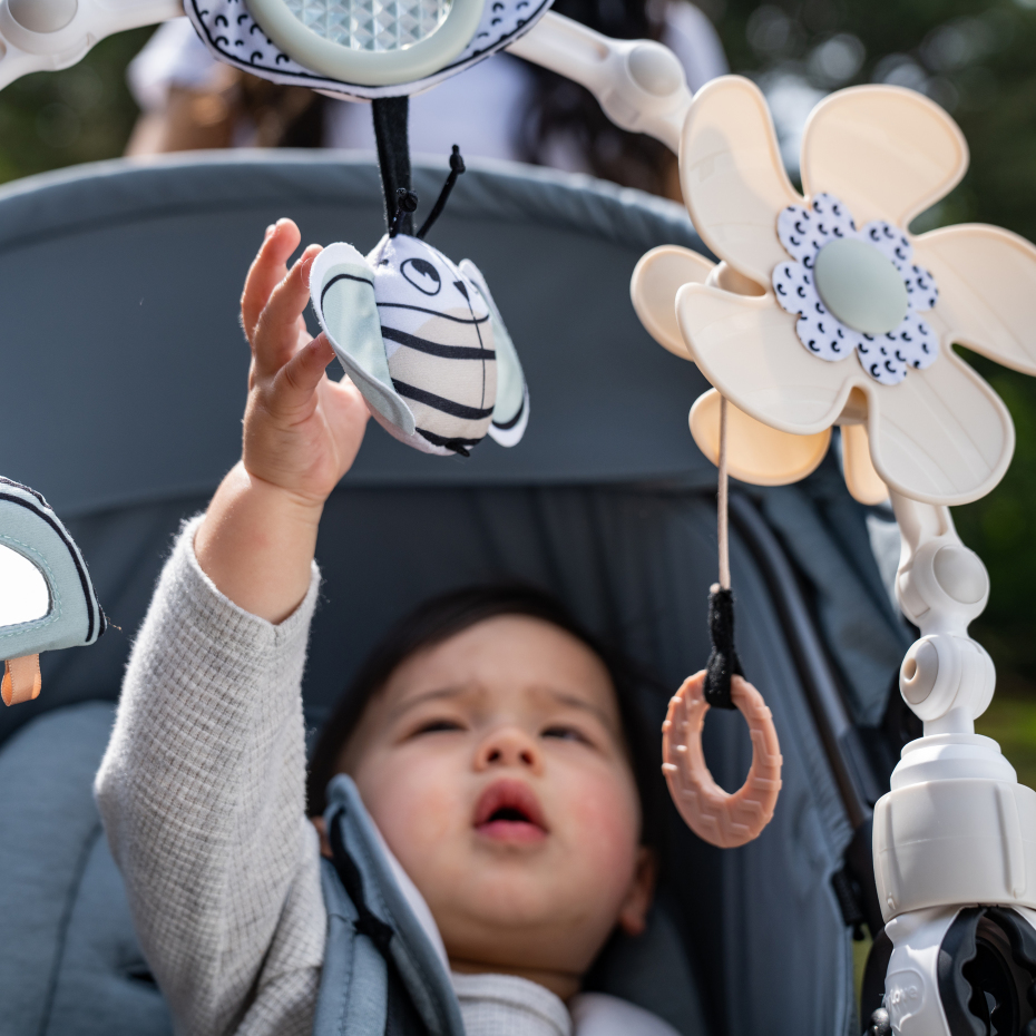 Criança no carrinho de bebé a tocar móbil com brinquedos coloridos