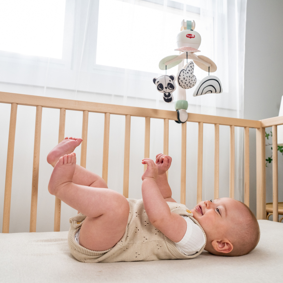 Bebé deitado em berço de madeira a olhar para móbile com figuras coloridas