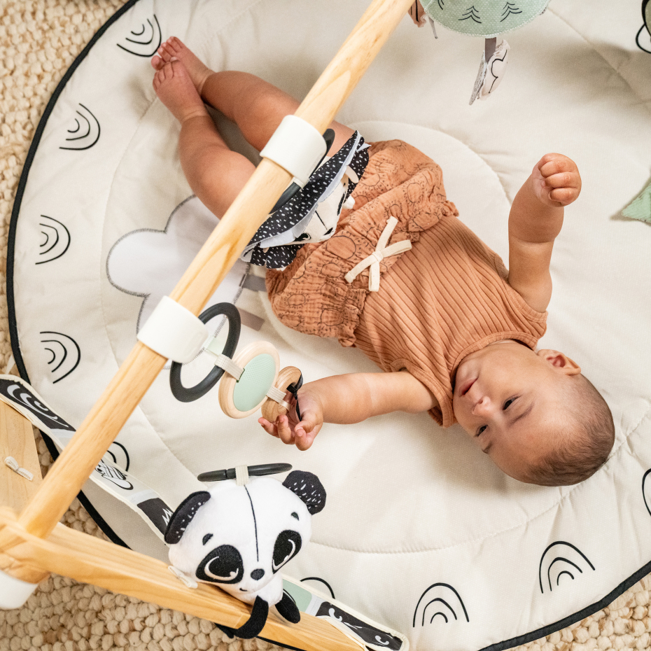 Tapete de atividades para bebé redondo bege com padrão de arcos pretos e brinquedos pendurados