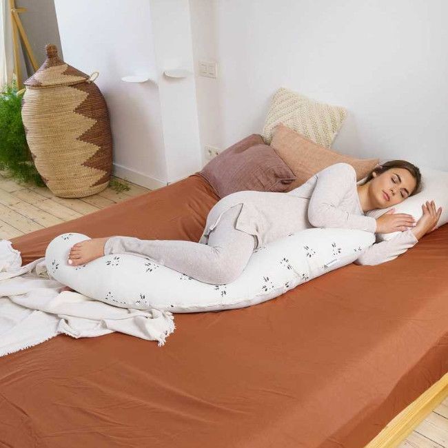 Mulher dormindo segurando almofada de corpo branca com flores numa cama com lençol castanho