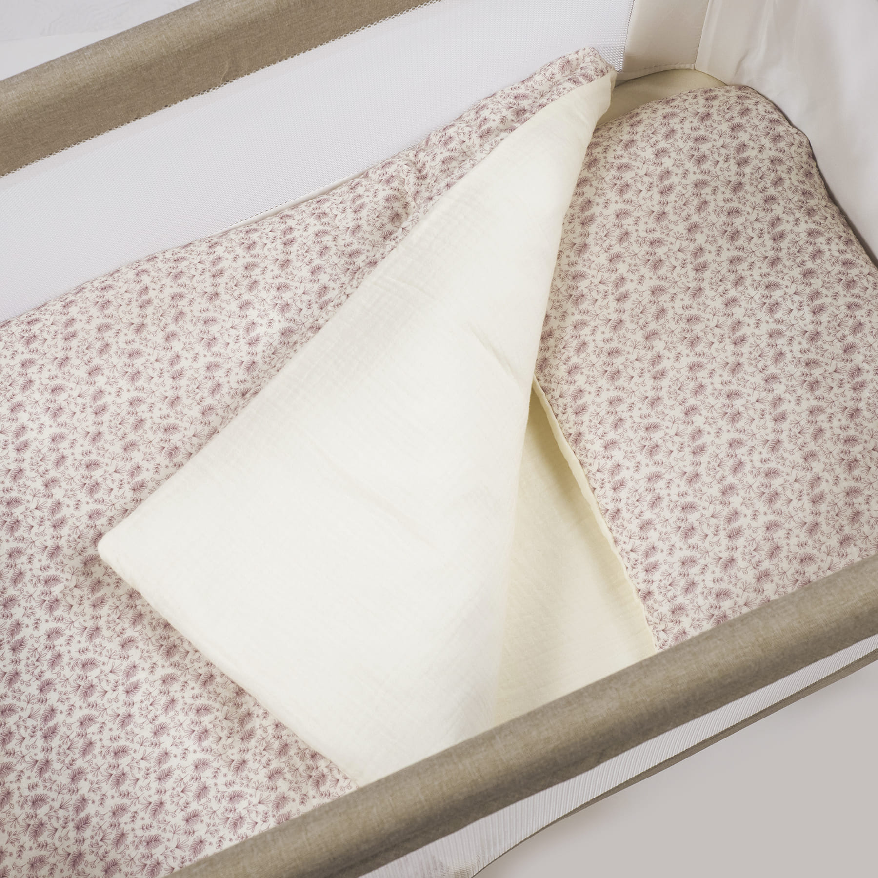 Berço com roupa de cama rosa clara floral e tecido branco