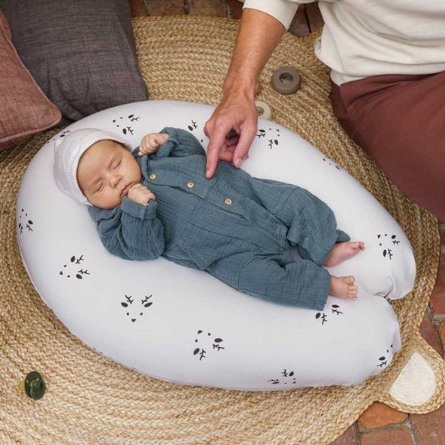 Almofada branca para bebé com padrão de folhas pretas, bebé vestido azul e touca branca a dormir