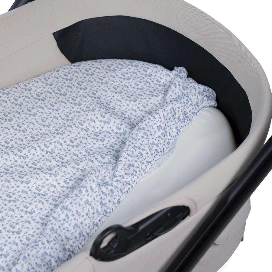 Berço portátil bege com colchão branco e lençol floral azul