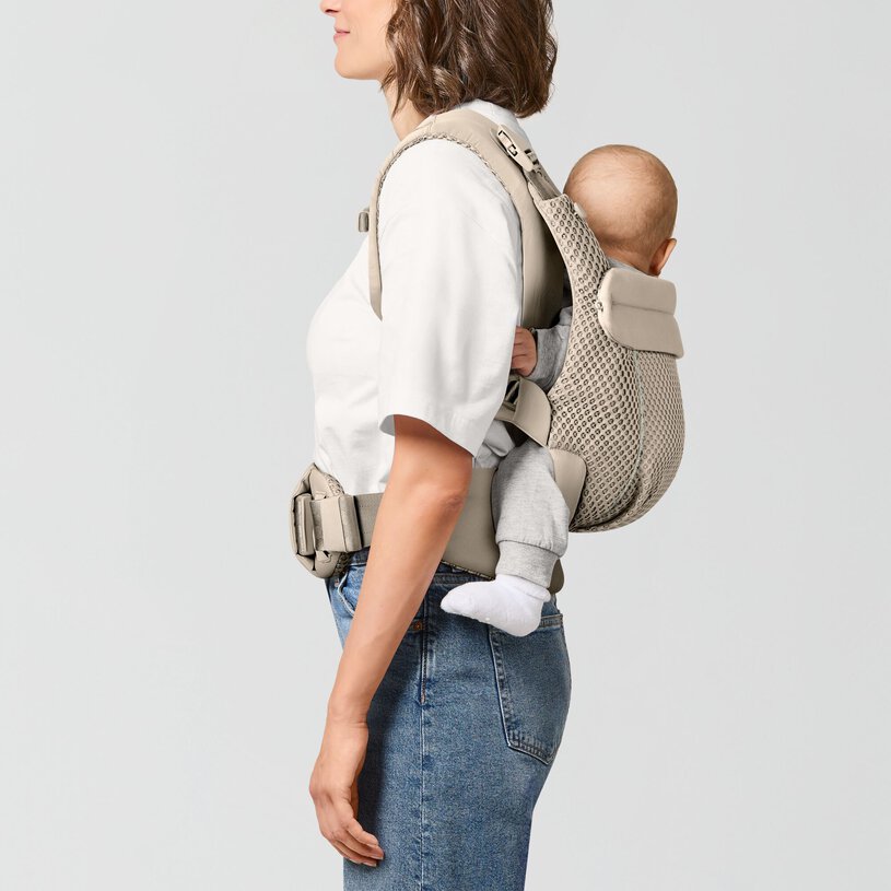 Mochila porta-bebé bege com bebé e mulher vista de perfil