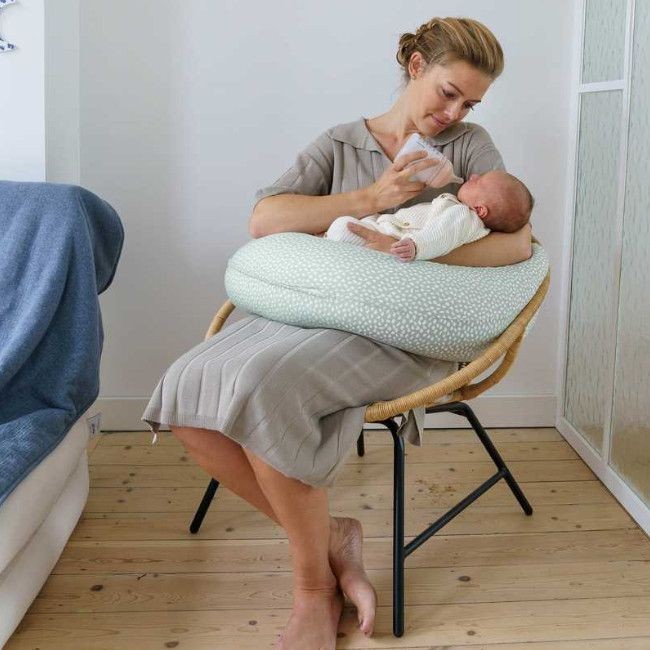 Mulher sentada com almofada de amamentação verde claro com padrão de pontos e bebé ao colo