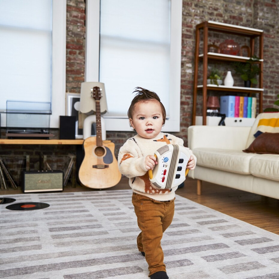Criança com brinquedo em sala com guitarra e estante