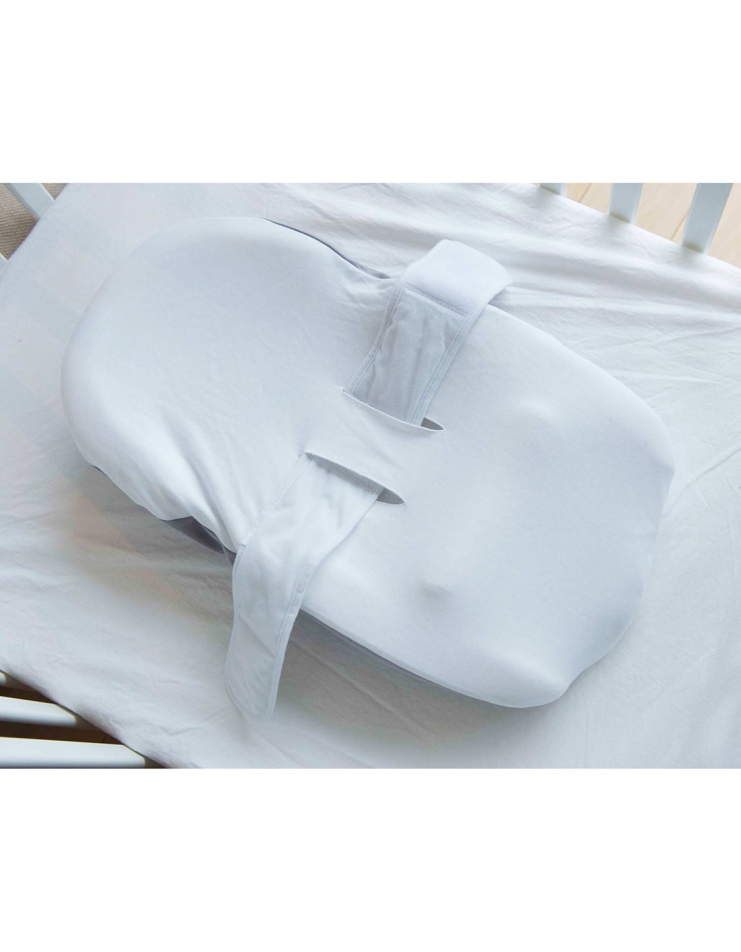 Almofada branca ergonómica para bebé com tiras ajustáveis colocada num berço branco