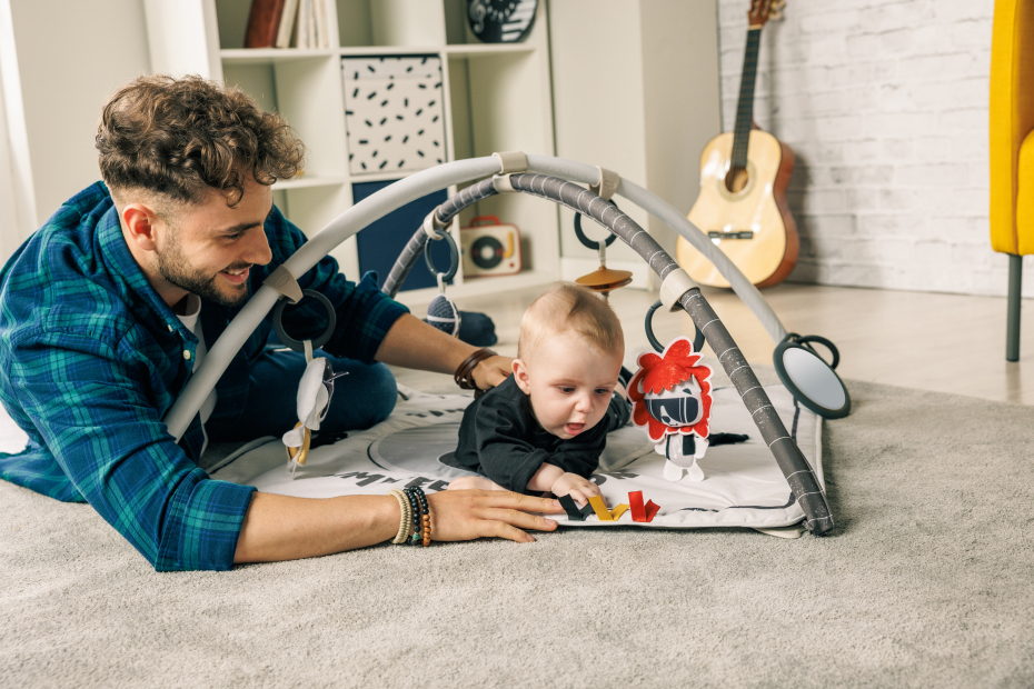 Tapete de atividades para bebé com arco cinzento e brinquedos coloridos, tapete cinzento, estante e guitarra ao fundo